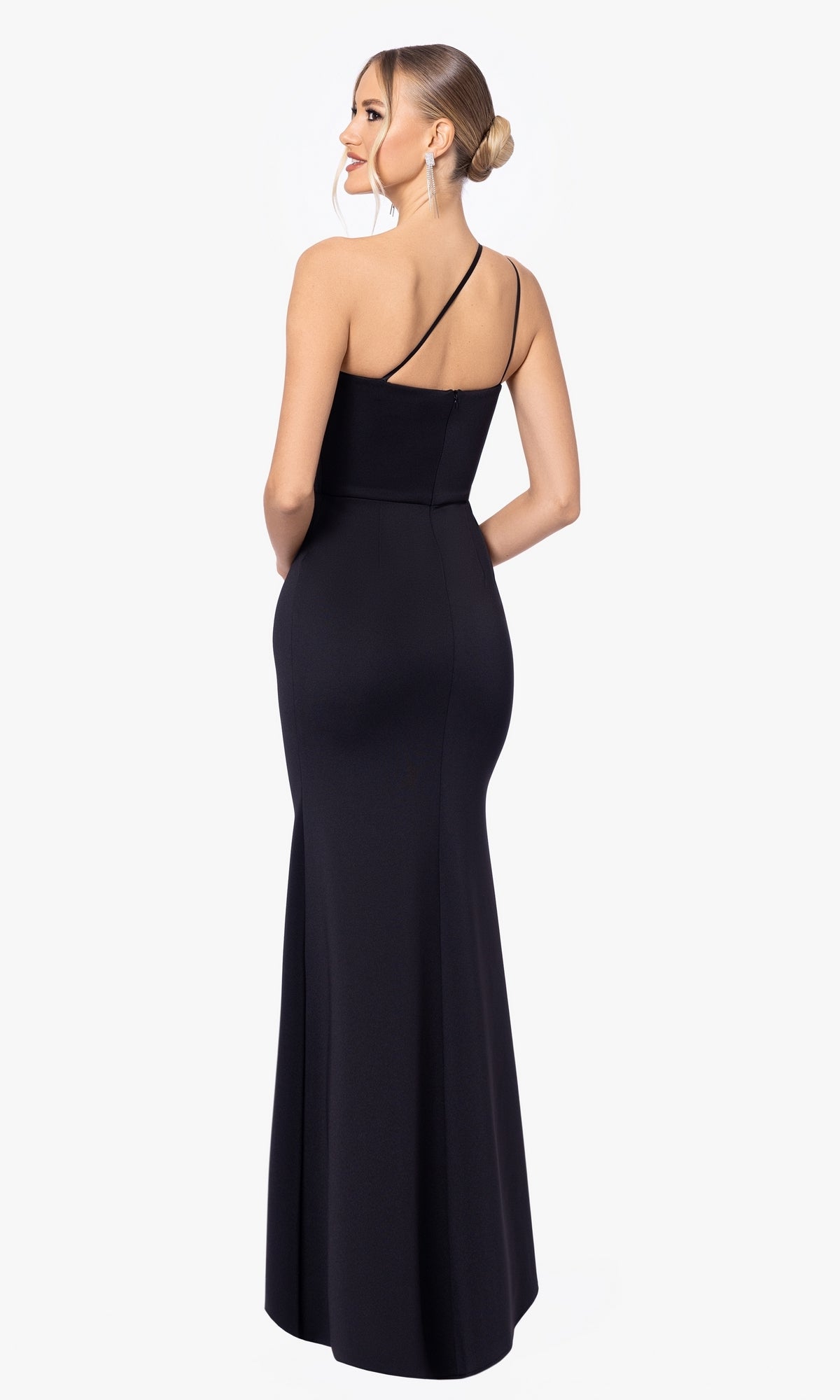 Woman models the Blondie Nites 5047BN, a long black prom dress with a fitted, one-shoulder design and an elegant low back, showcasing the stunning floor-length formal gown from behind.